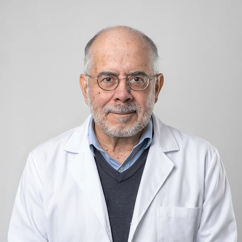 Portrait of a senior male doctor wearing a white lab coat and glasses, facing the camera.
